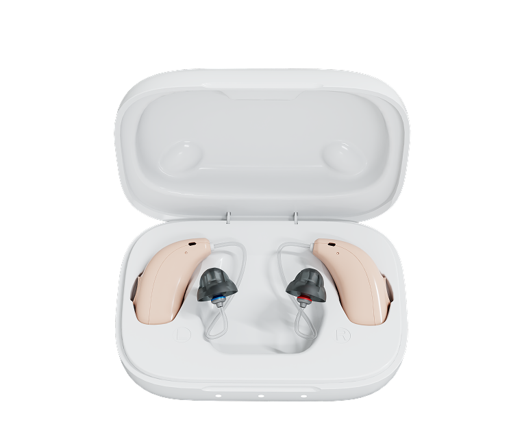 A pair of beige behind-the-ear hearing aids with dark gray ear tips, displayed inside an open white charging case on a solid white background.